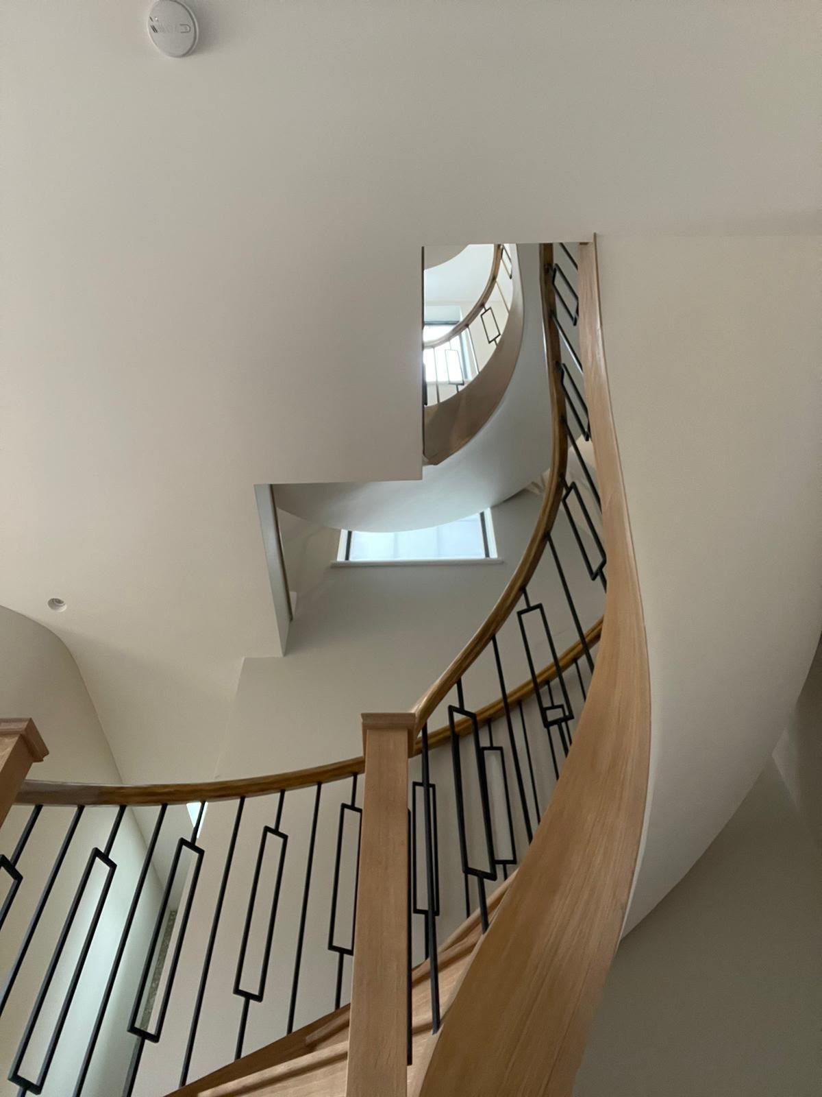 Timber handrail and black geometric balusters rising through a curved stairwell