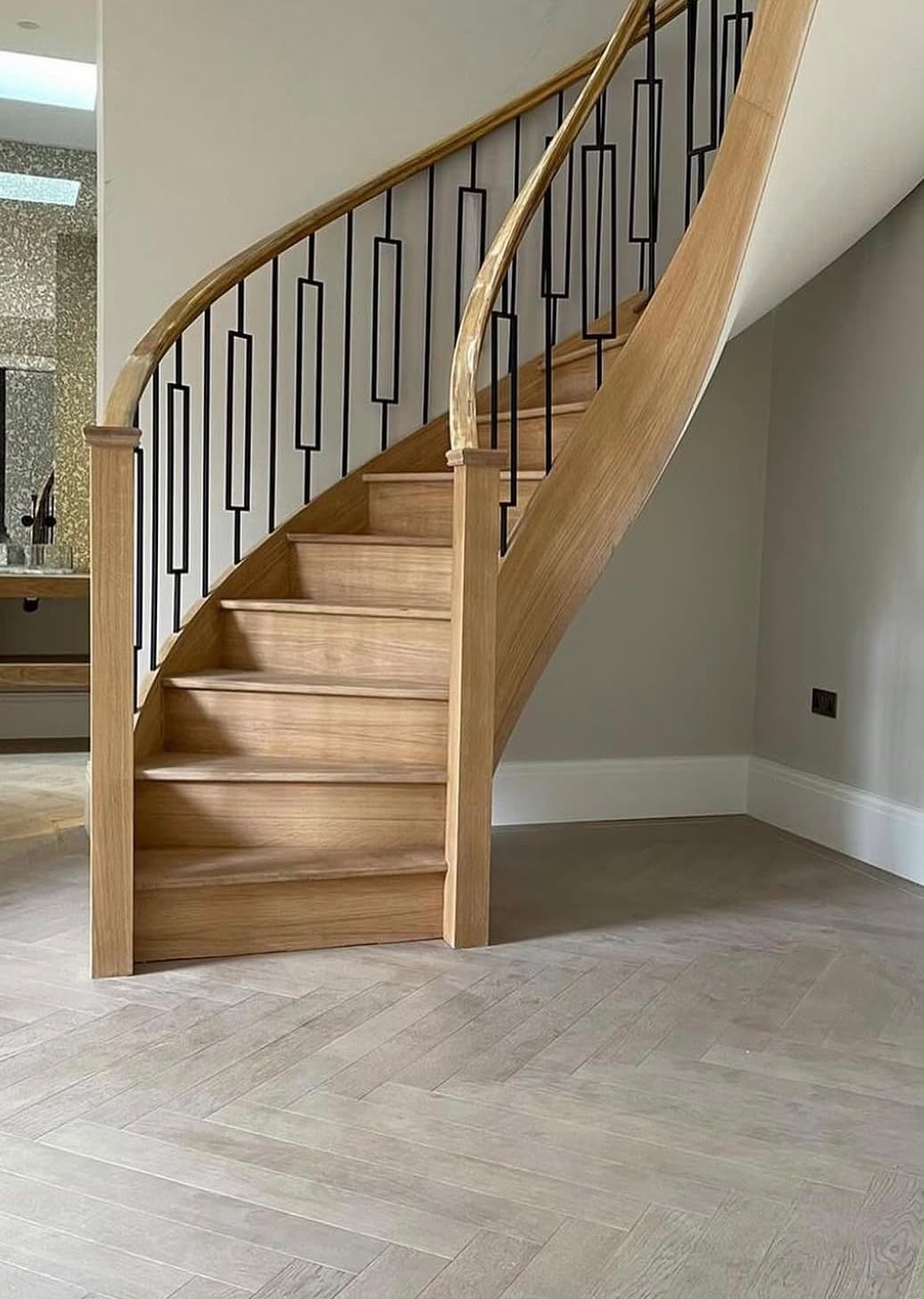 Curved timber staircase with black geometric balusters and a timber handrail