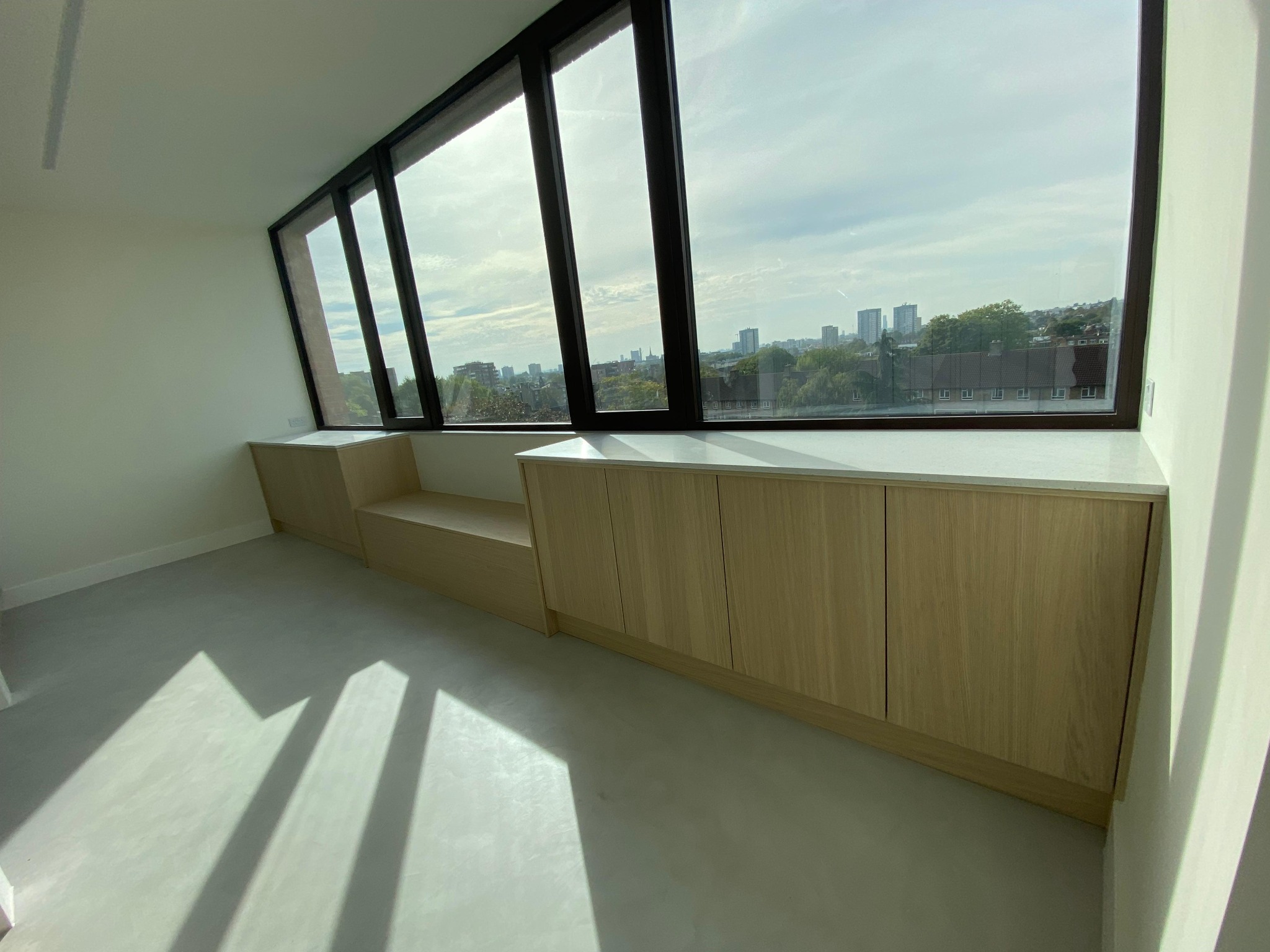 Long fitted timber storage unit beneath office windows